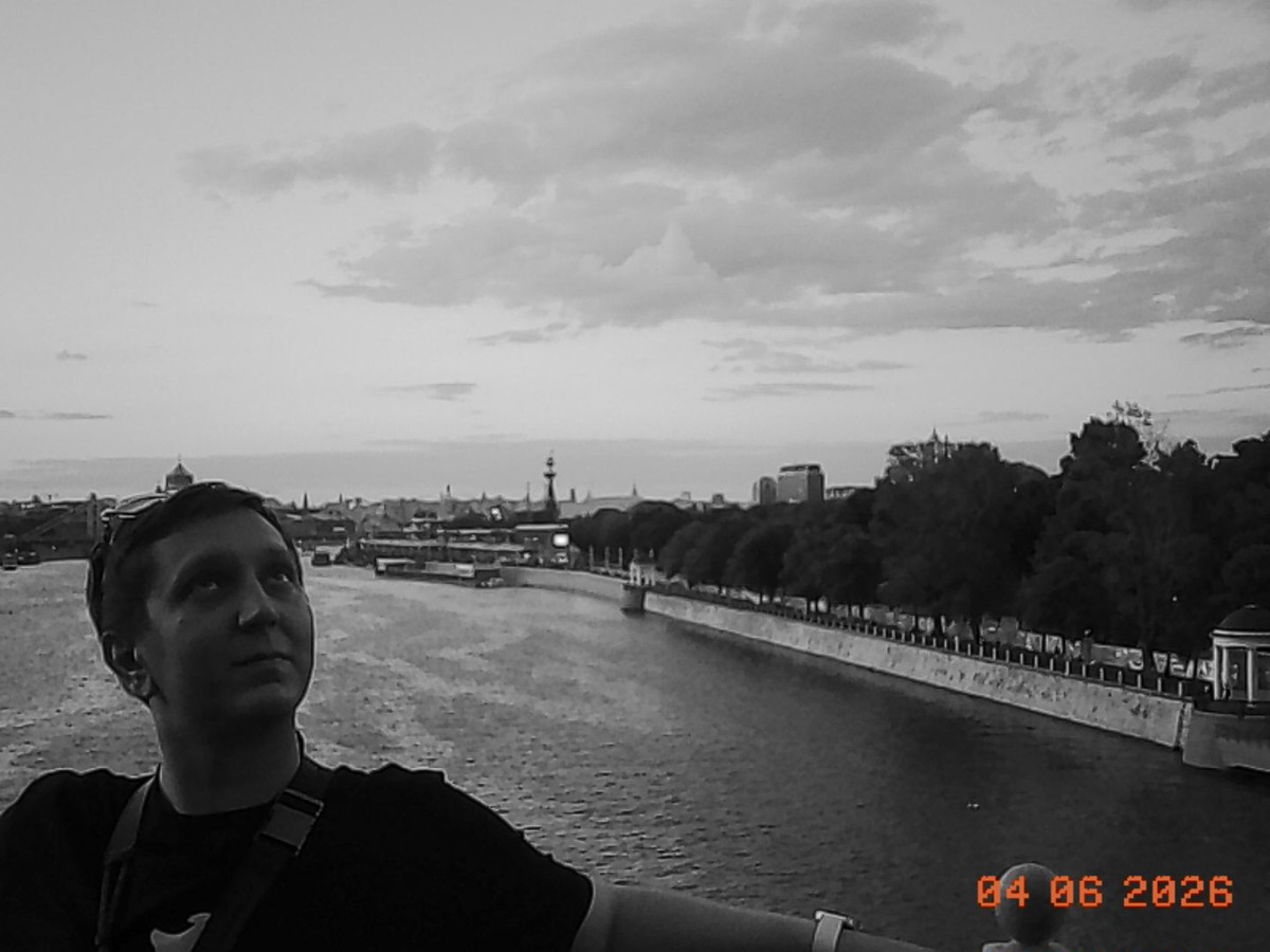 Black-and-white self-portrait above a city river, shot on Charmera