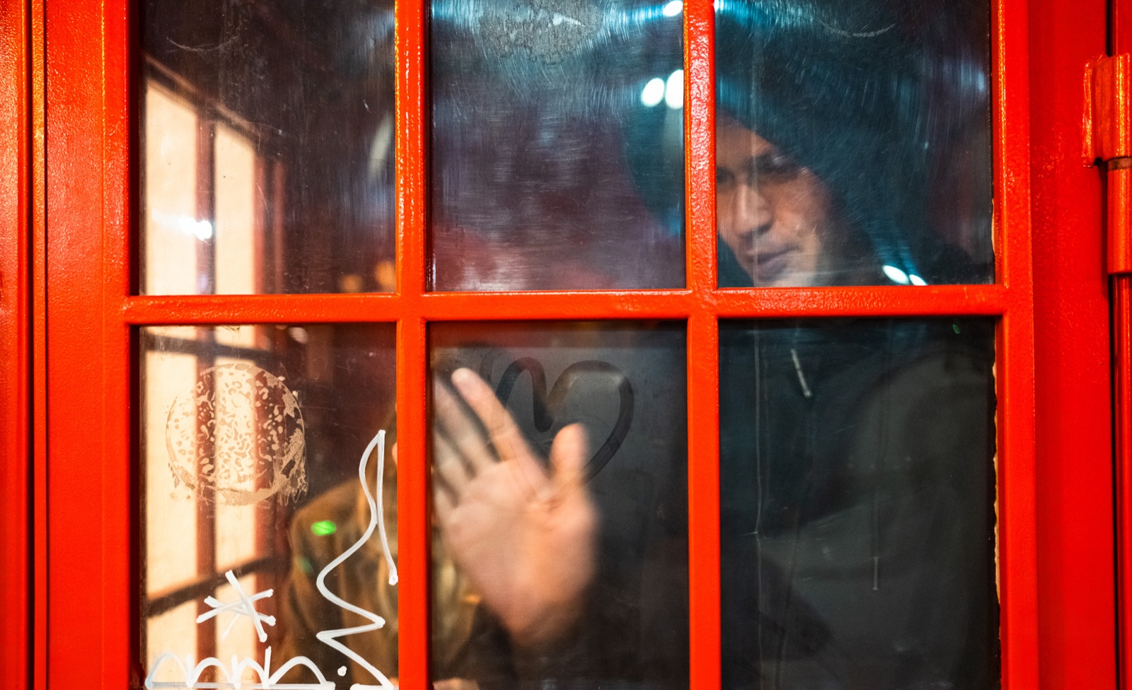 A man behind the glass of a red phone booth